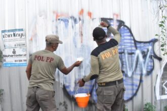 Personel Satpol PP Surabaya melakukan pembersihan tembok yang menjadi salah satu sasaran aksi vandalisme, Jumat (7/2/2025) | Foto: dok. Satpol PP Surabaya