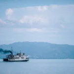 Ilustrasi: Kapal penyebrangan melintas di perairan dengan latar pegunungan | Sumber Foto: Pixabay